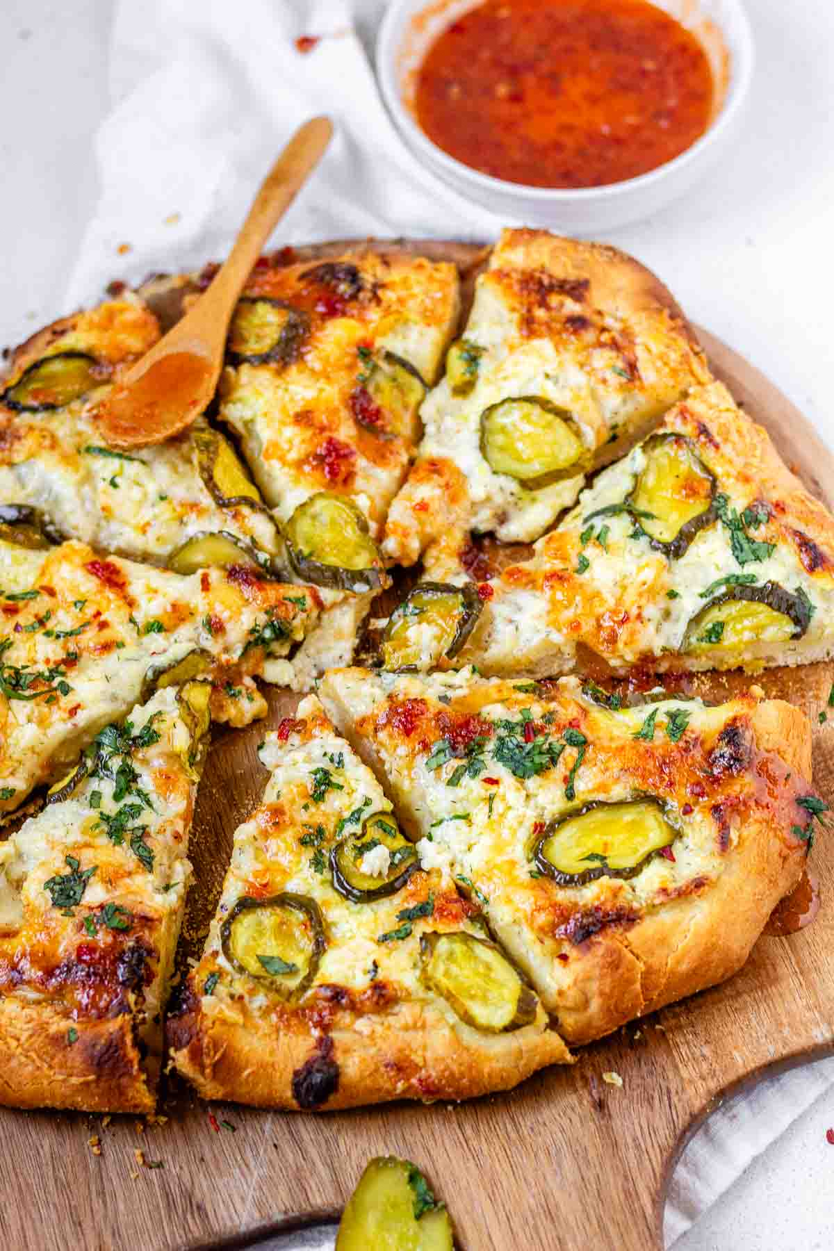 Pizza on a pizza peel topped with pickles and a red sauce.