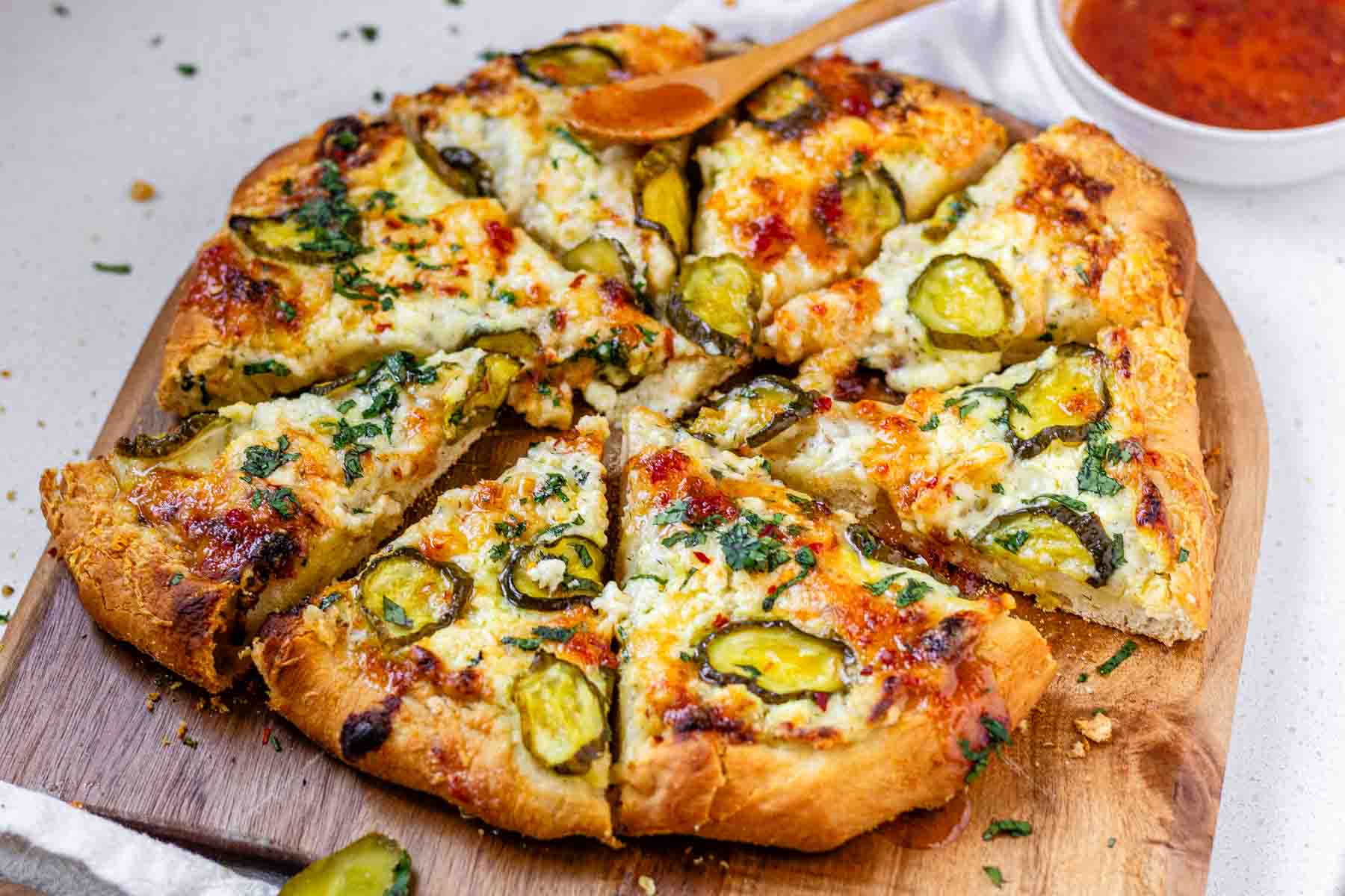 Pizza on a pizza peel topped with pickles and a red sauce.