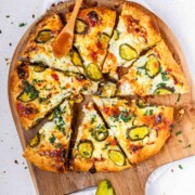 Pizza on a pizza peel topped with pickles and a red sauce.