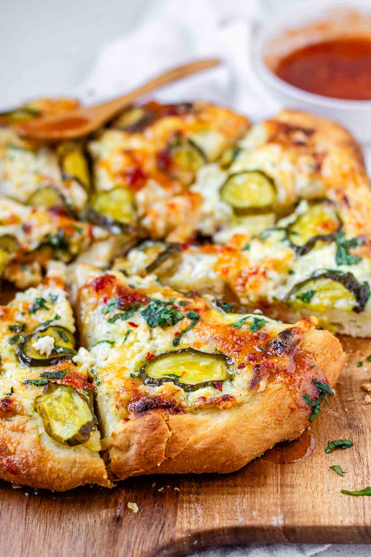 Pizza on a pizza peel topped with pickles and a red sauce.