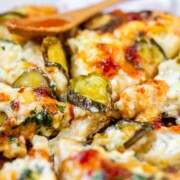 Pizza on a pizza peel topped with pickles and a red sauce.