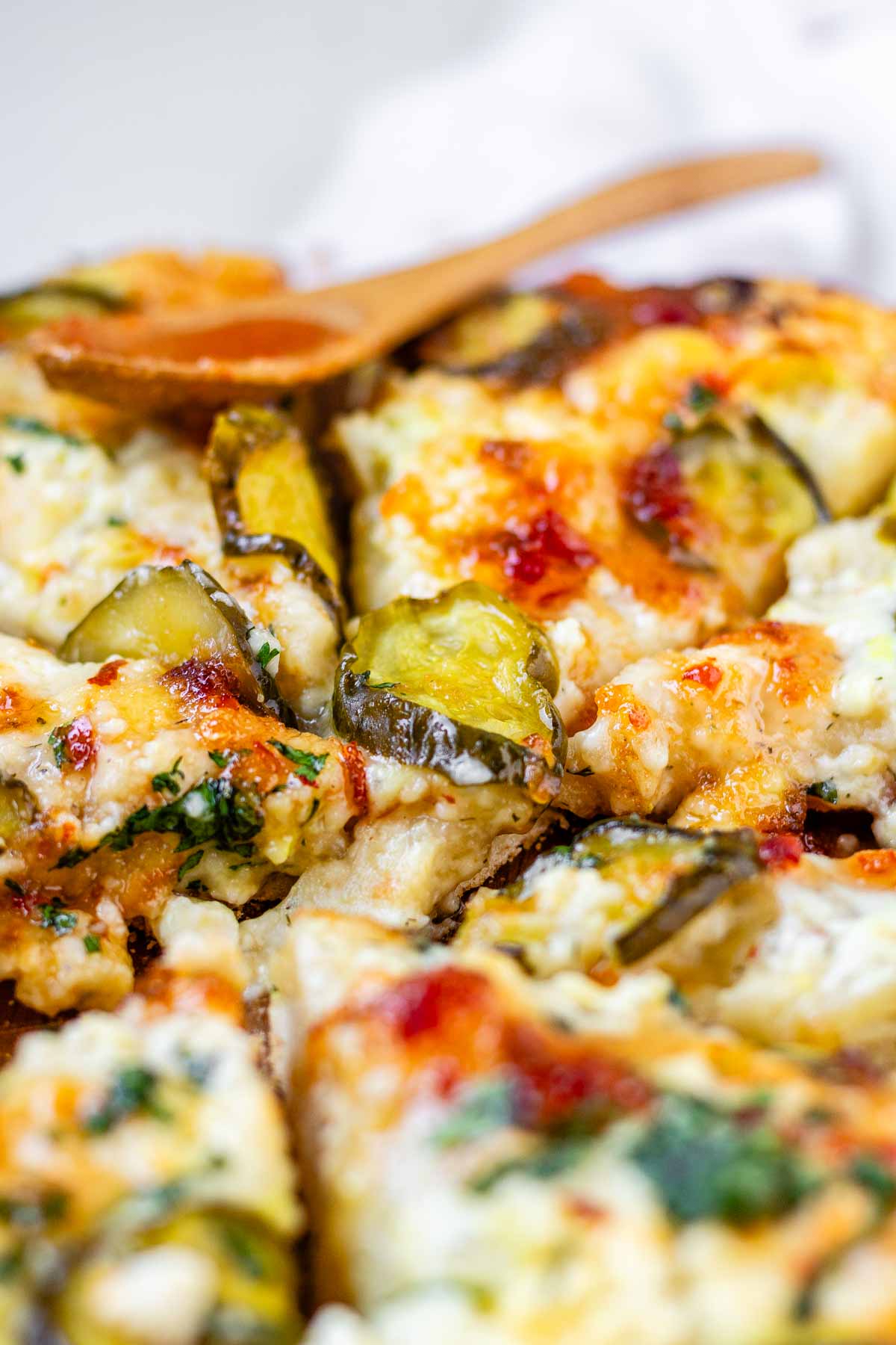 Pizza on a pizza peel topped with pickles and a red sauce.