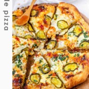 Pizza on a pizza peel topped with pickles and a red sauce with the text pickle pizza.