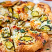 Pizza on a pizza peel topped with pickles and a red sauce with the text pickle pizza.