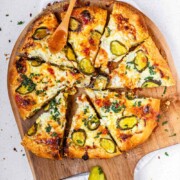 Pizza on a pizza peel topped with pickles and a red sauce with the text pickle pizza.