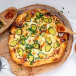 Pizza on a pizza peel topped with pickles and a red sauce.