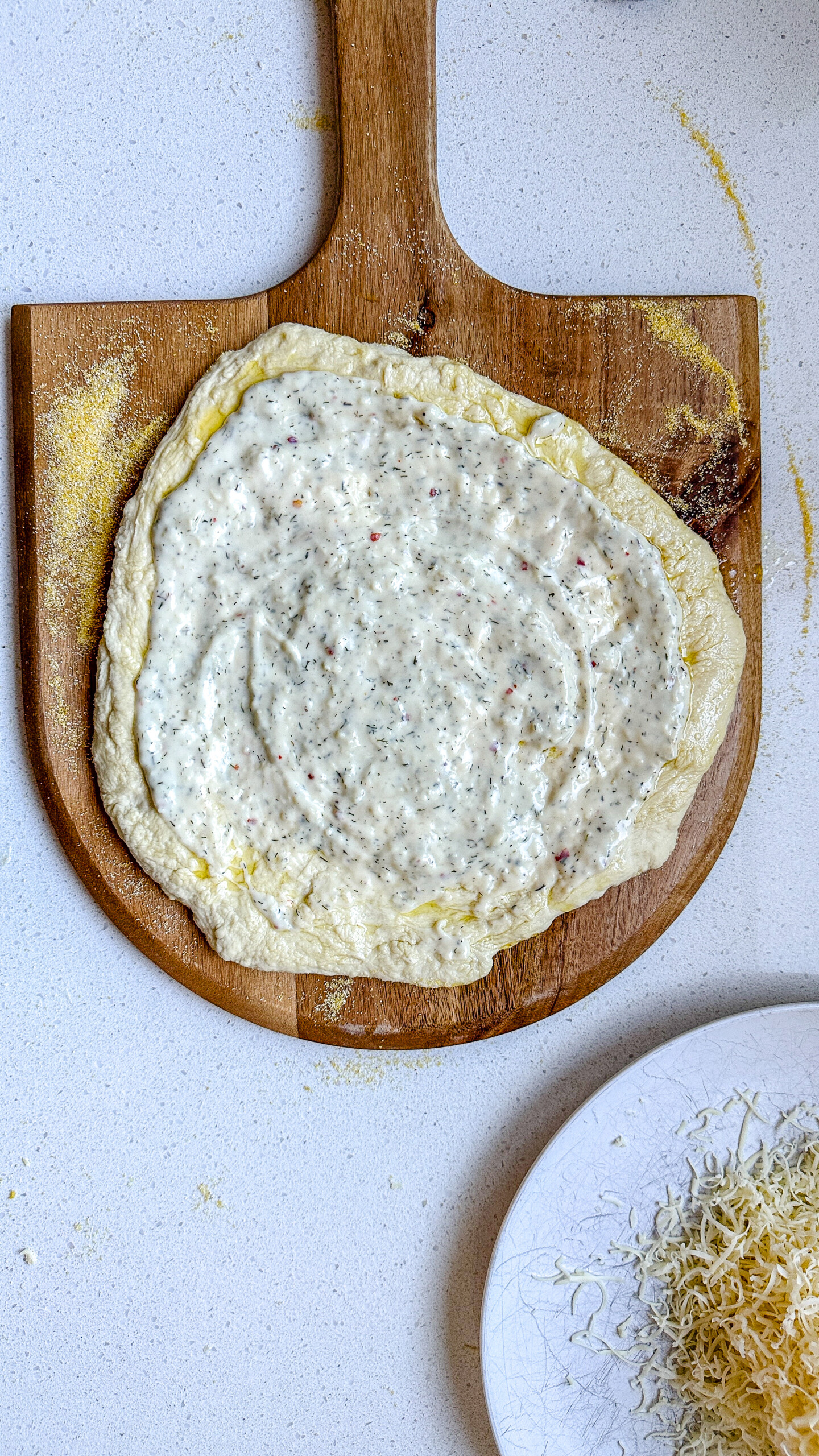 Pizza dough on a pizza peel topped with white sauce.
