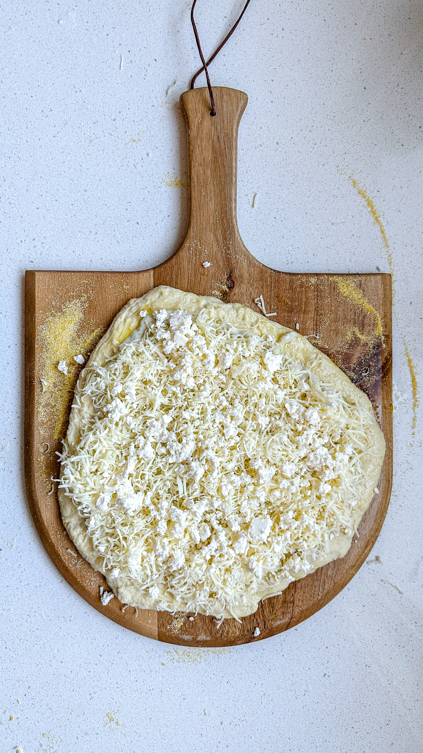 Pizza dough on a pizza peel topped with white sauce and white cheese.