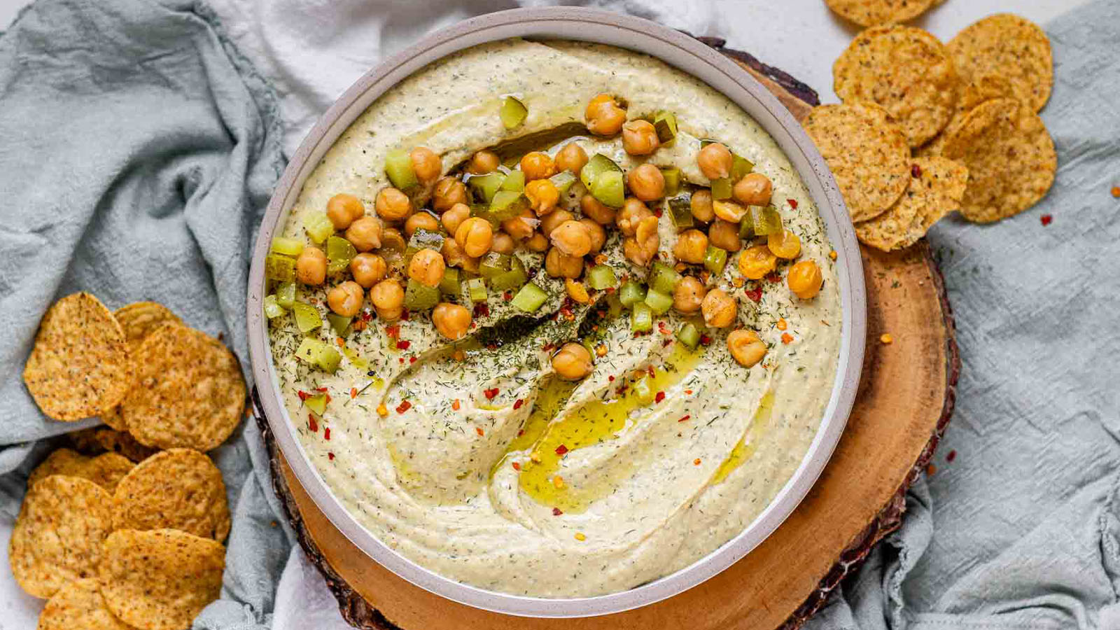 Hummus in a bowl topped with olive oil, chickpeas, chopped pickles, and spices.