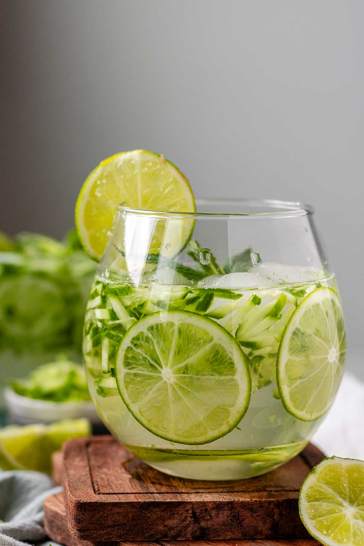 A drink in a glass garnished with julienned cucumber, lime slices, and a sprig of mint.