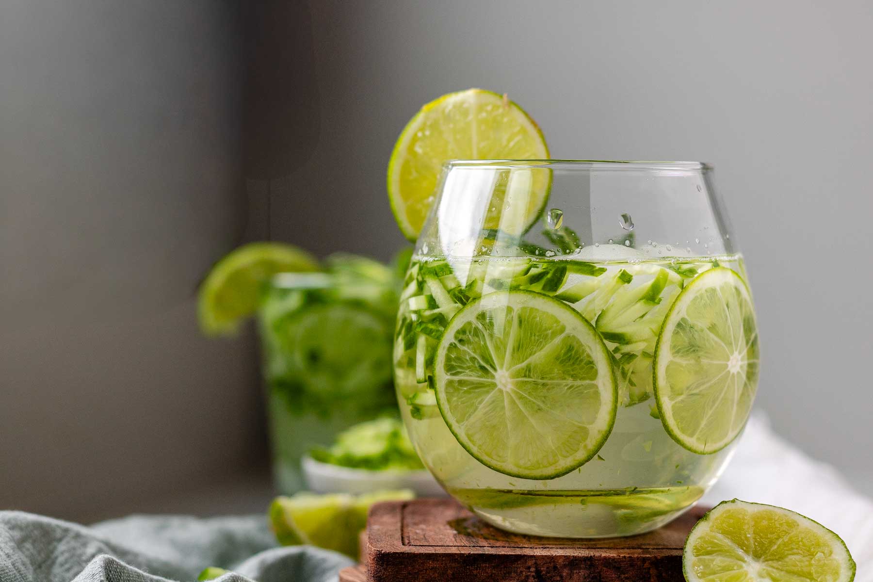 A drink in a glass garnished with julienned cucumber, lime slices, and a sprig of mint.