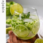 A drink in a glass garnished with julienned cucumber, lime slices, and a sprig of mint with the text sekajabin.