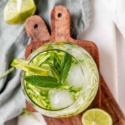 A drink in a glass garnished with julienned cucumber, lime slices, and a sprig of mint with the text sekajabin.