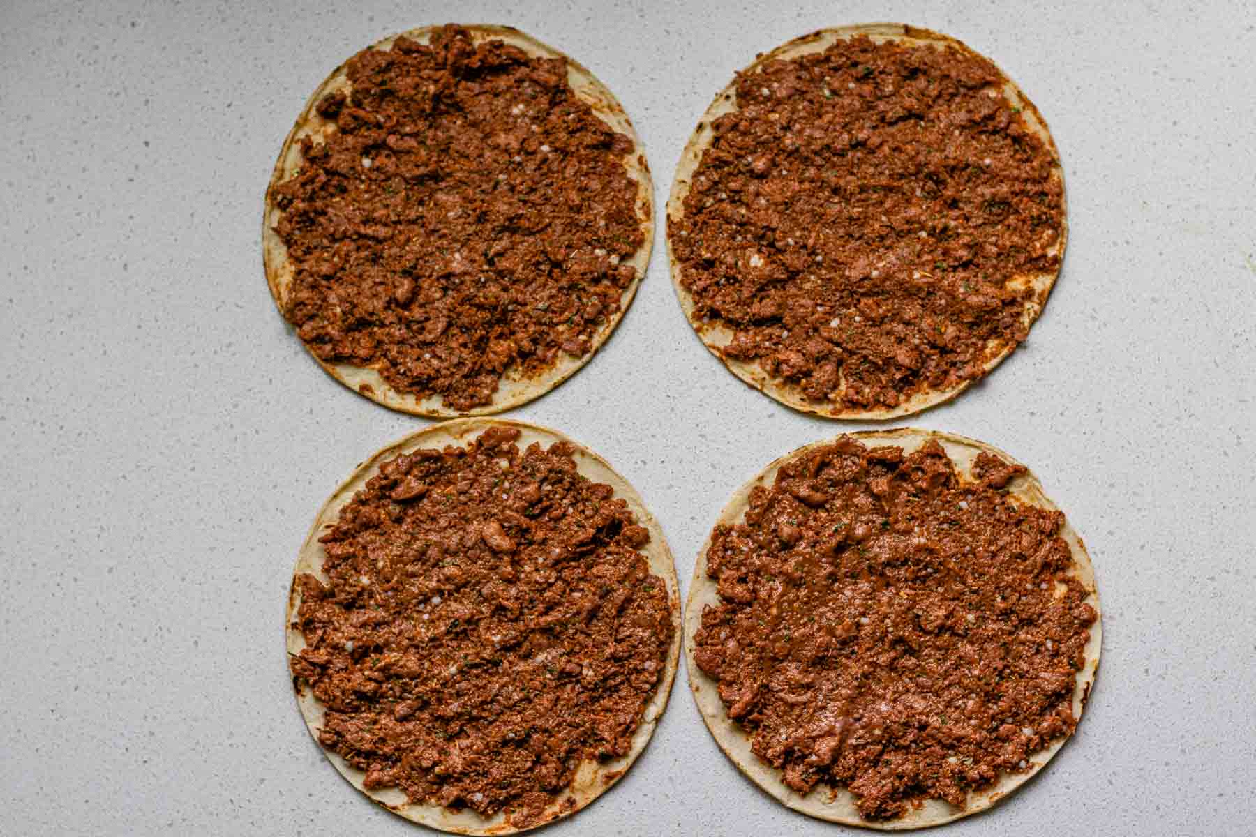 Corn tortillas covered in uncooked plant-based meat.
