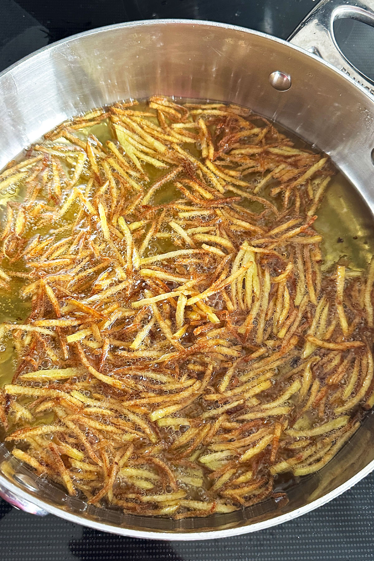 Thin shoestring fries frying in a skillet of oil.