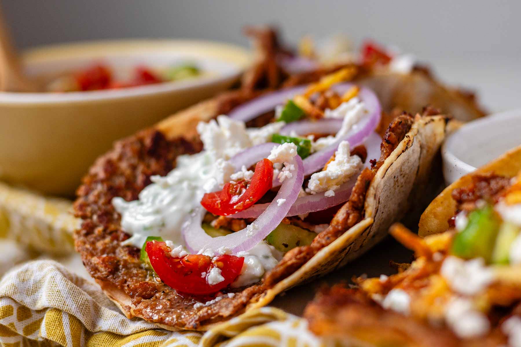 Tacos filled with meat, tomato, cucumber, red onion, feta, white sauce, and shoestring fries.
