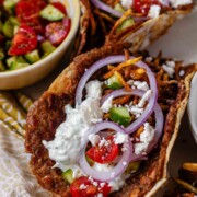 Tacos filled with meat, tomato, cucumber, red onion, feta, white sauce, and shoestring fries.