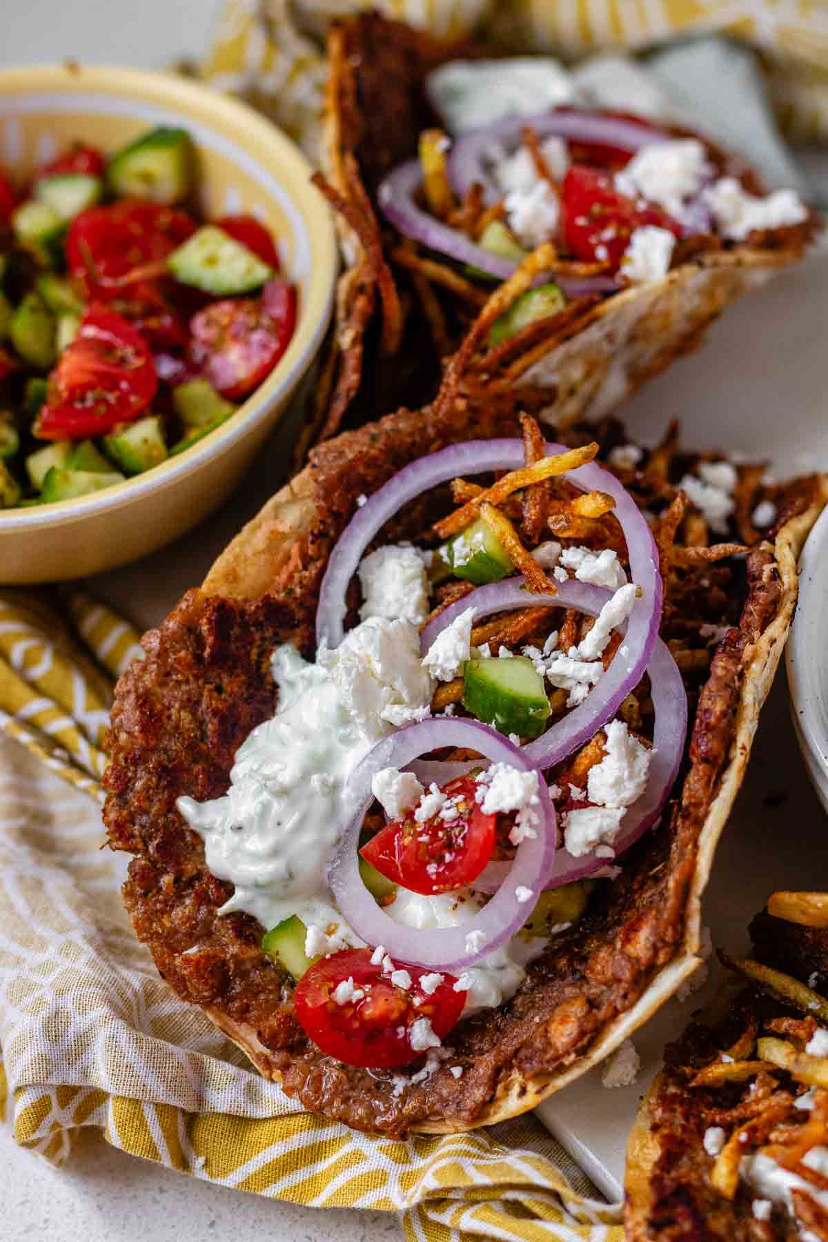 Tacos filled with meat, tomato, cucumber, red onion, feta, white sauce, and shoestring fries.