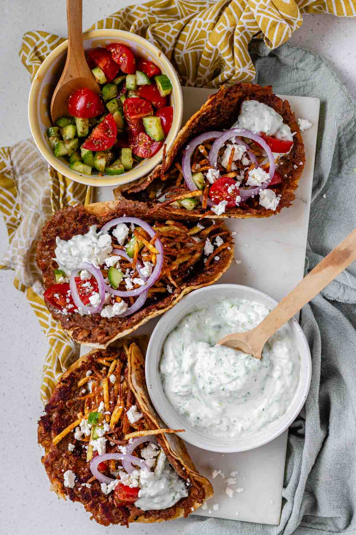 Tacos filled with meat, tomato, cucumber, red onion, feta, white sauce, and shoestring fries.
