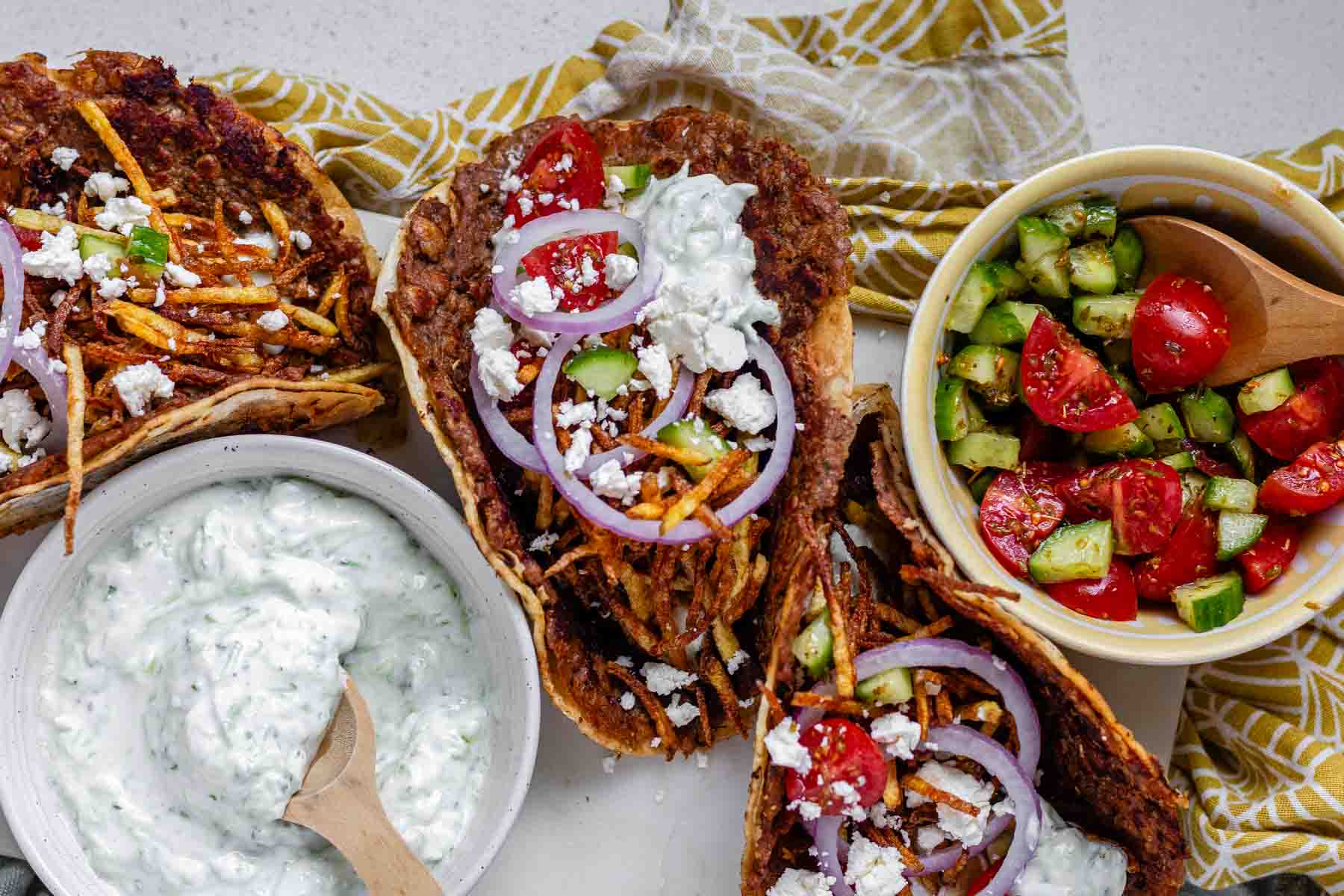 Tacos filled with meat, tomato, cucumber, red onion, feta, white sauce, and shoestring fries.