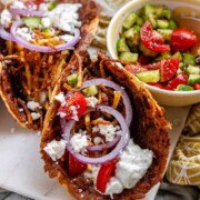Tacos filled with meat, tomato, cucumber, red onion, feta, white sauce, and shoestring fries.