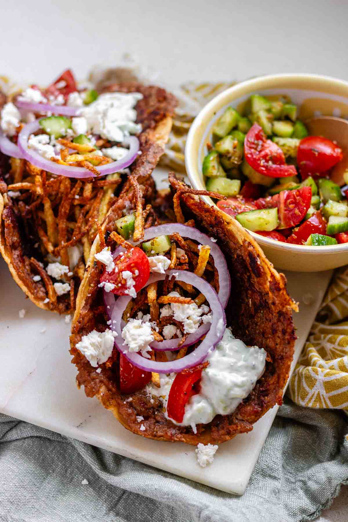 Tacos filled with meat, tomato, cucumber, red onion, feta, white sauce, and shoestring fries.