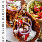 Tacos filled with meat, tomato, cucumber, red onion, feta, white sauce, and shoestring fries with the text Greek-Inspired Smash Tacos.