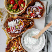 Tacos filled with meat, tomato, cucumber, red onion, feta, white sauce, and shoestring fries with the text Greek-Inspired Smash Tacos.