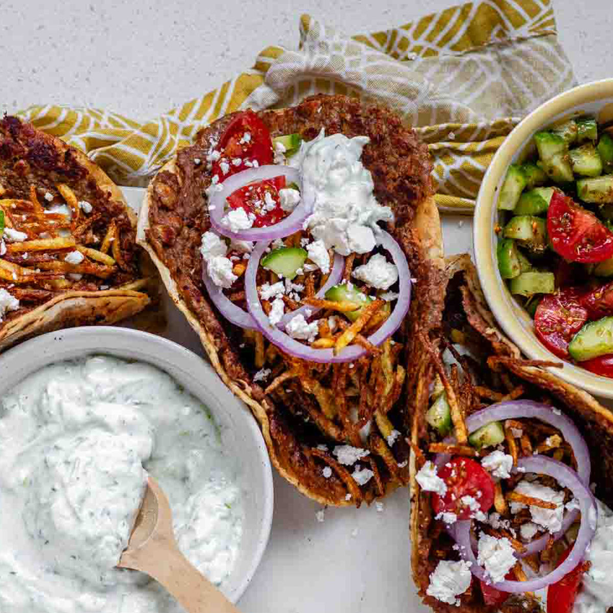 Tacos filled with meat, tomato, cucumber, red onion, feta, white sauce, and shoestring fries.