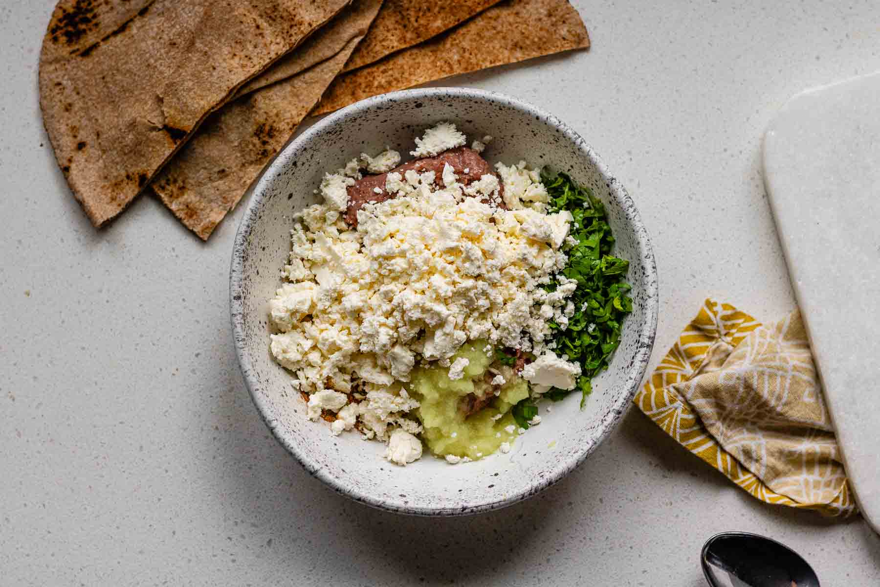 A bowl with ground meat, feta cheese, grated onion, and fresh grated parsley.