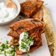 A stack of meat-filled fried pitas with tzatziki sauce and fresh parsley on top.