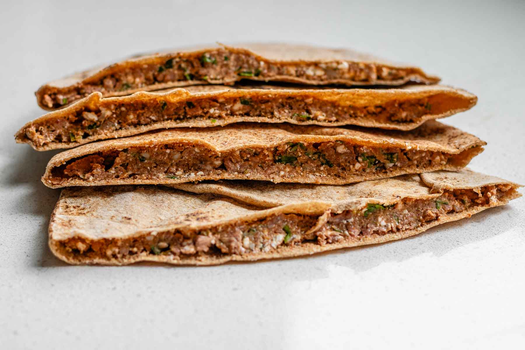 A stack of uncooked meat-filled pitas.