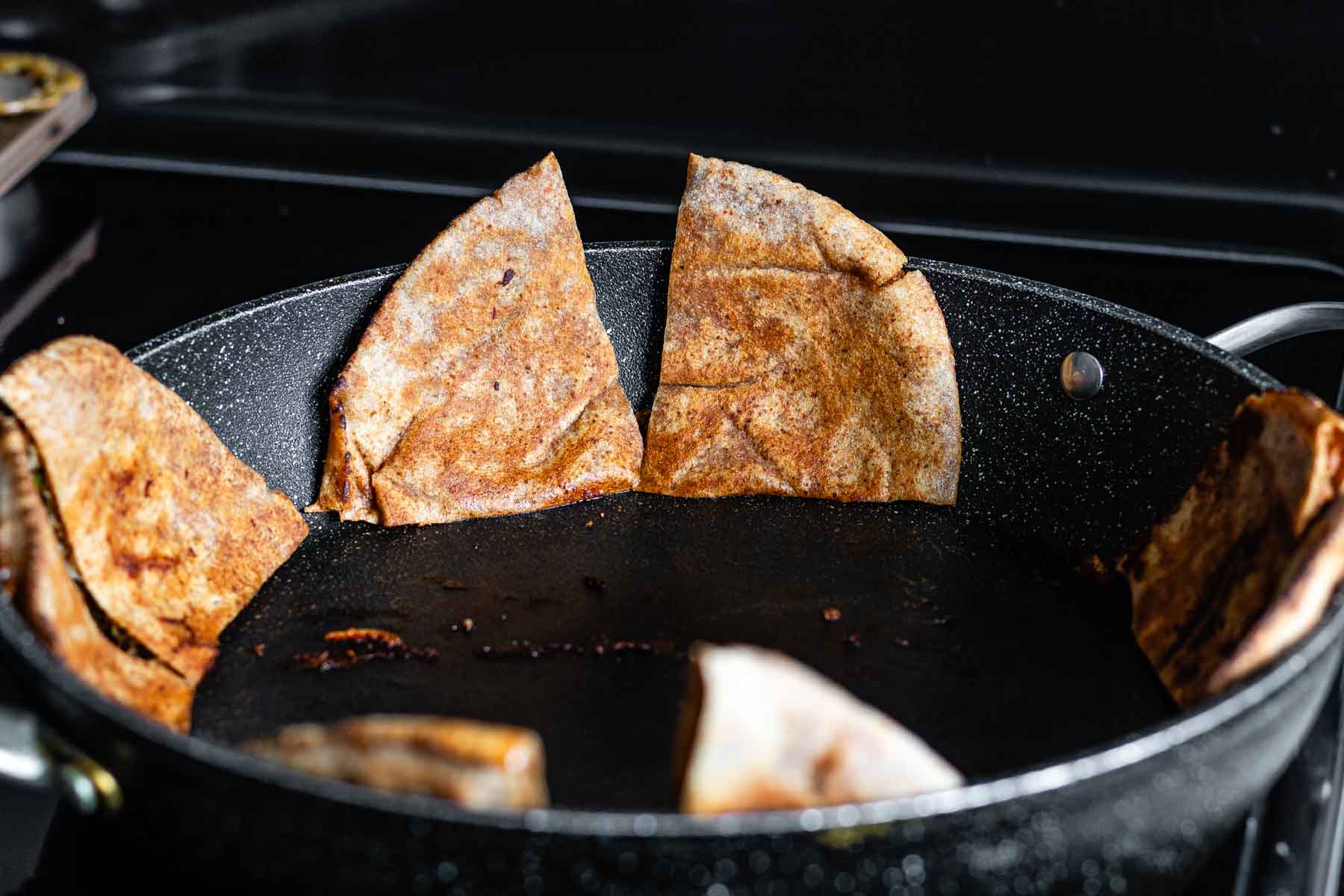 Stuffed quartered pitas frying in a pan.