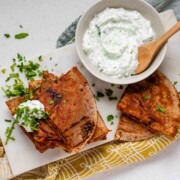 A stack of meat-filled fried pitas with tzatziki sauce and fresh parsley on top.