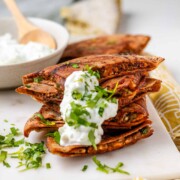 A stack of meat-filled fried pitas with tzatziki sauce and fresh parsley on top.