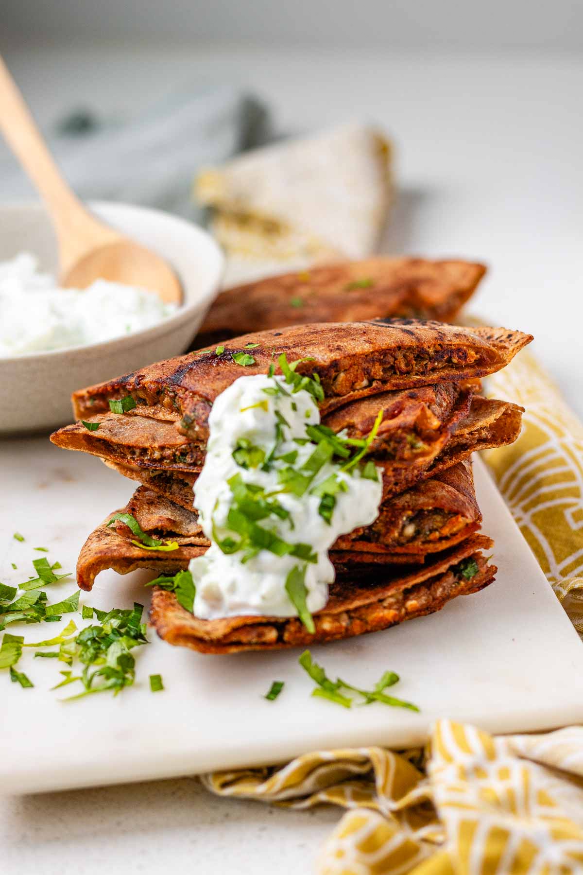 A stack of meat-filled fried pitas with tzatziki sauce and fresh parsley on top.