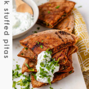 A stack of meat-filled fried pitas with tzatziki sauce and fresh parsley on top, with the text Greek stuffed pitas.
