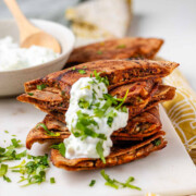 A stack of meat-filled fried pitas with tzatziki sauce and fresh parsley on top, with the text Greek Inspired stuffed pitas.