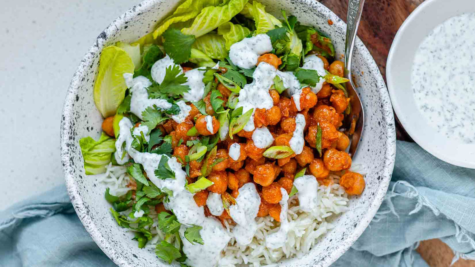A bowl with rice, chickpeas, salad and a white sauce.