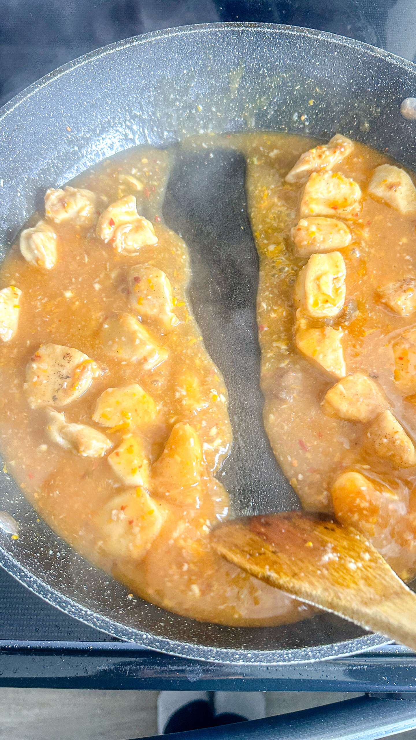Cubed chicken in orange sauce in a skillet.