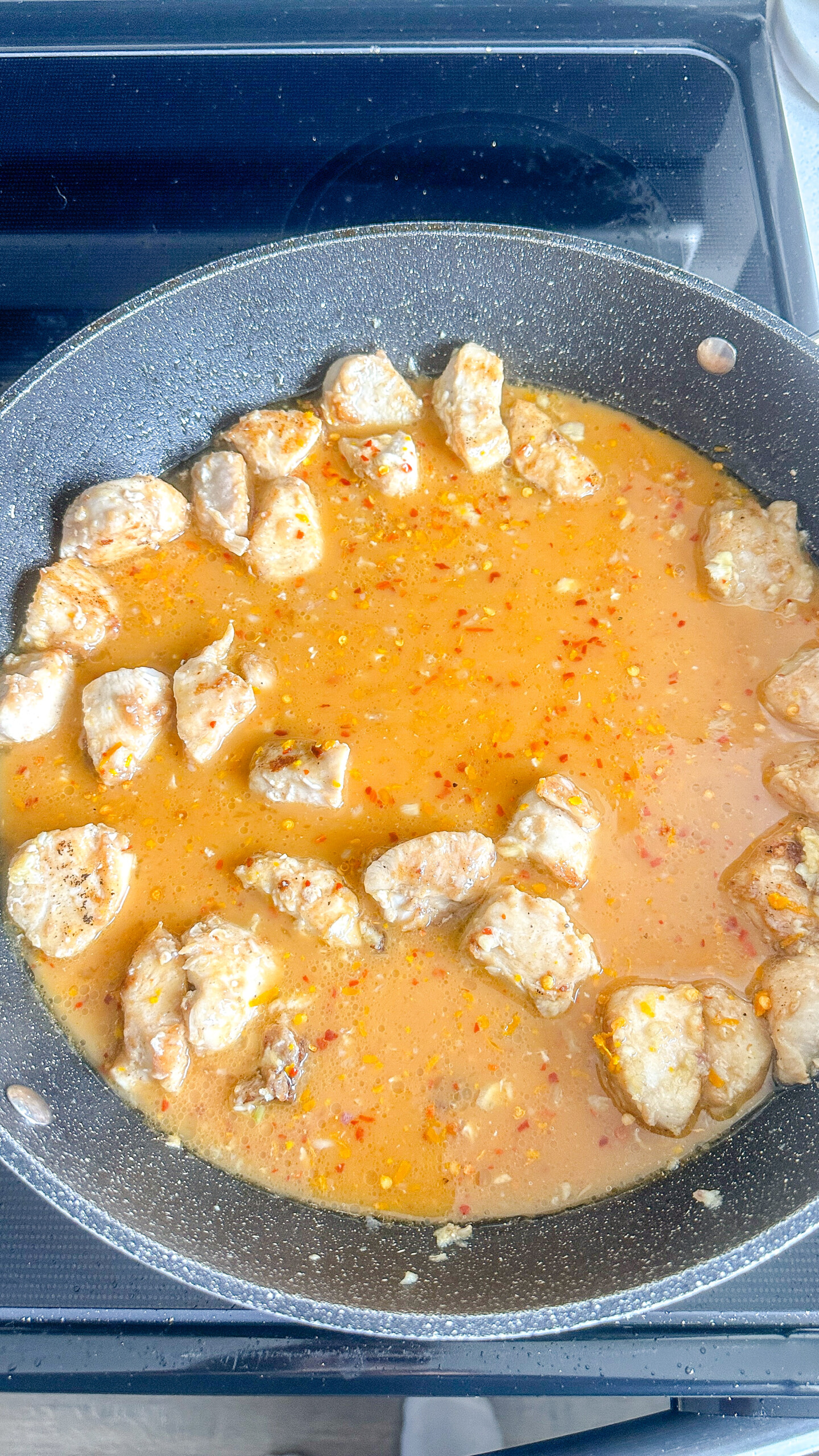 Cubed chicken in orange sauce in a skillet.