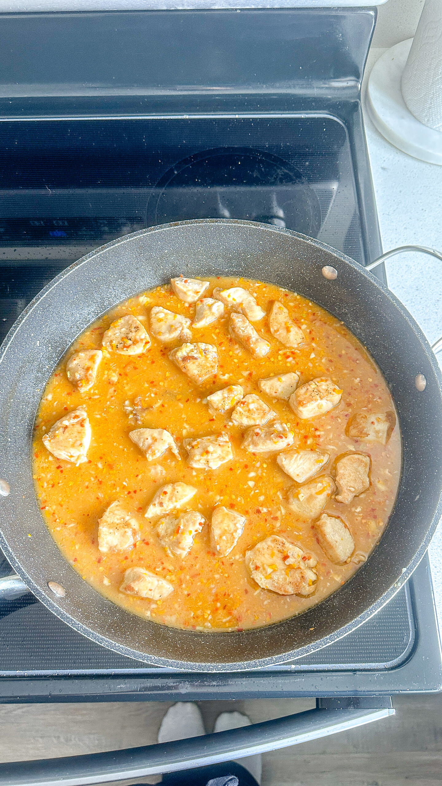 Cubed chicken in orange sauce in a skillet.