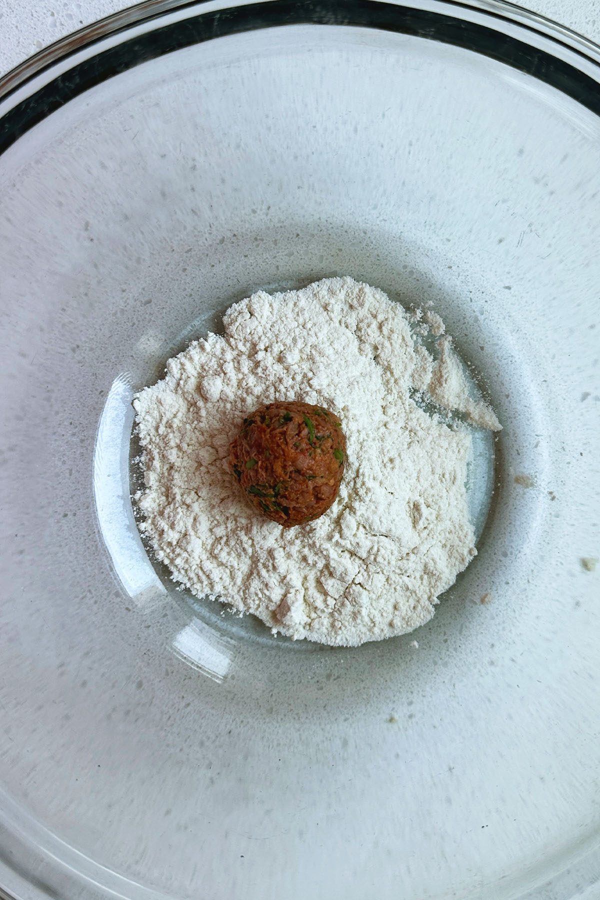 A rolled meatball sitting in a bowl of flour.