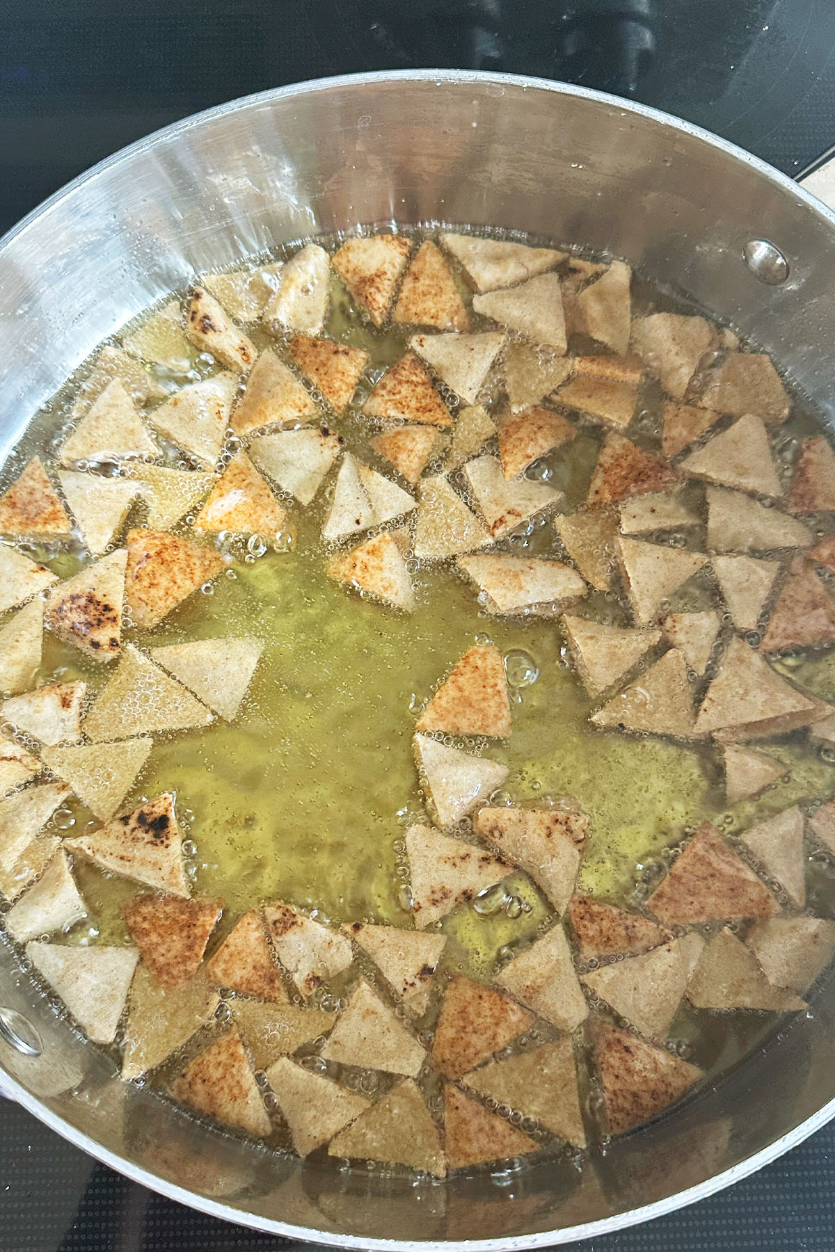 Pita triangles frying in a skillet of oil.