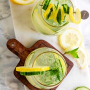A cocktail garnished with lemon and cucumber slices and fresh mint.