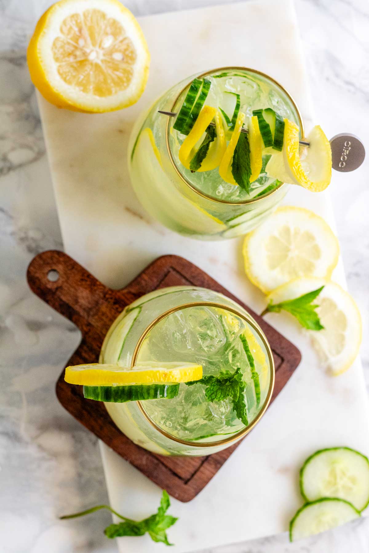 A cocktail garnished with lemon and cucumber slices and fresh mint.