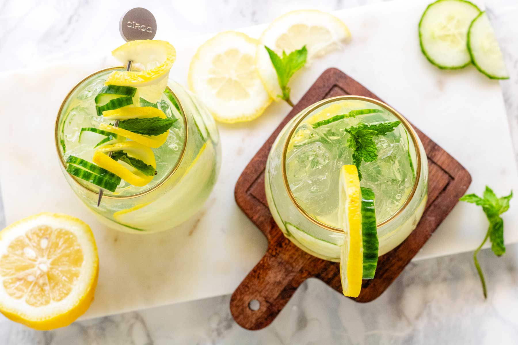 A cocktail garnished with lemon and cucumber slices and fresh mint.