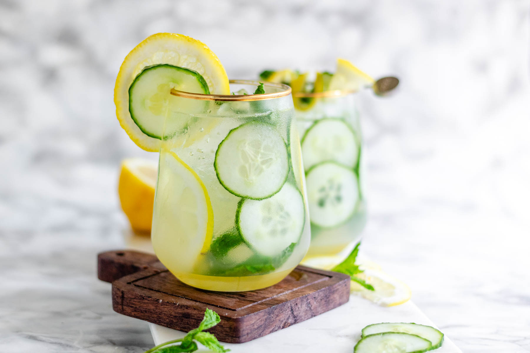 A cocktail garnished with lemon and cucumber slices and fresh mint.