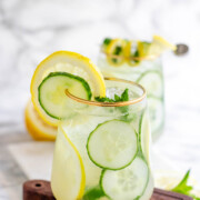 A cocktail garnished with lemon and cucumber slices and fresh mint.
