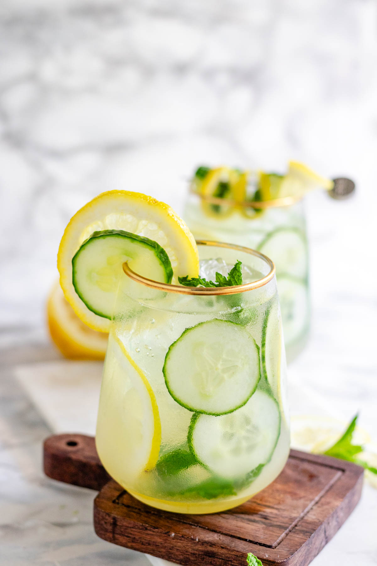 A cocktail garnished with lemon and cucumber slices and fresh mint.